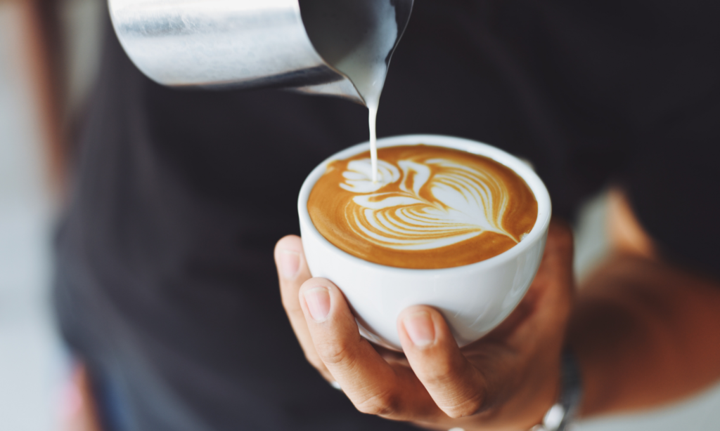 espresso coffee in a white coffee mug with barista pouring hot creme in the coffee in the decorative pattern of a flower