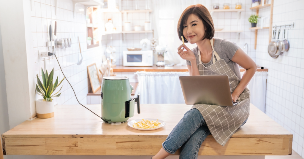 lady sitting on counter with her laptop eating french fries from an air fryer