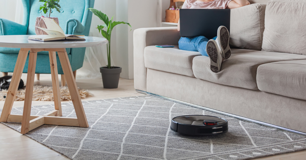 robot vacuum cleaning rug while woman sitting on couch with laptop